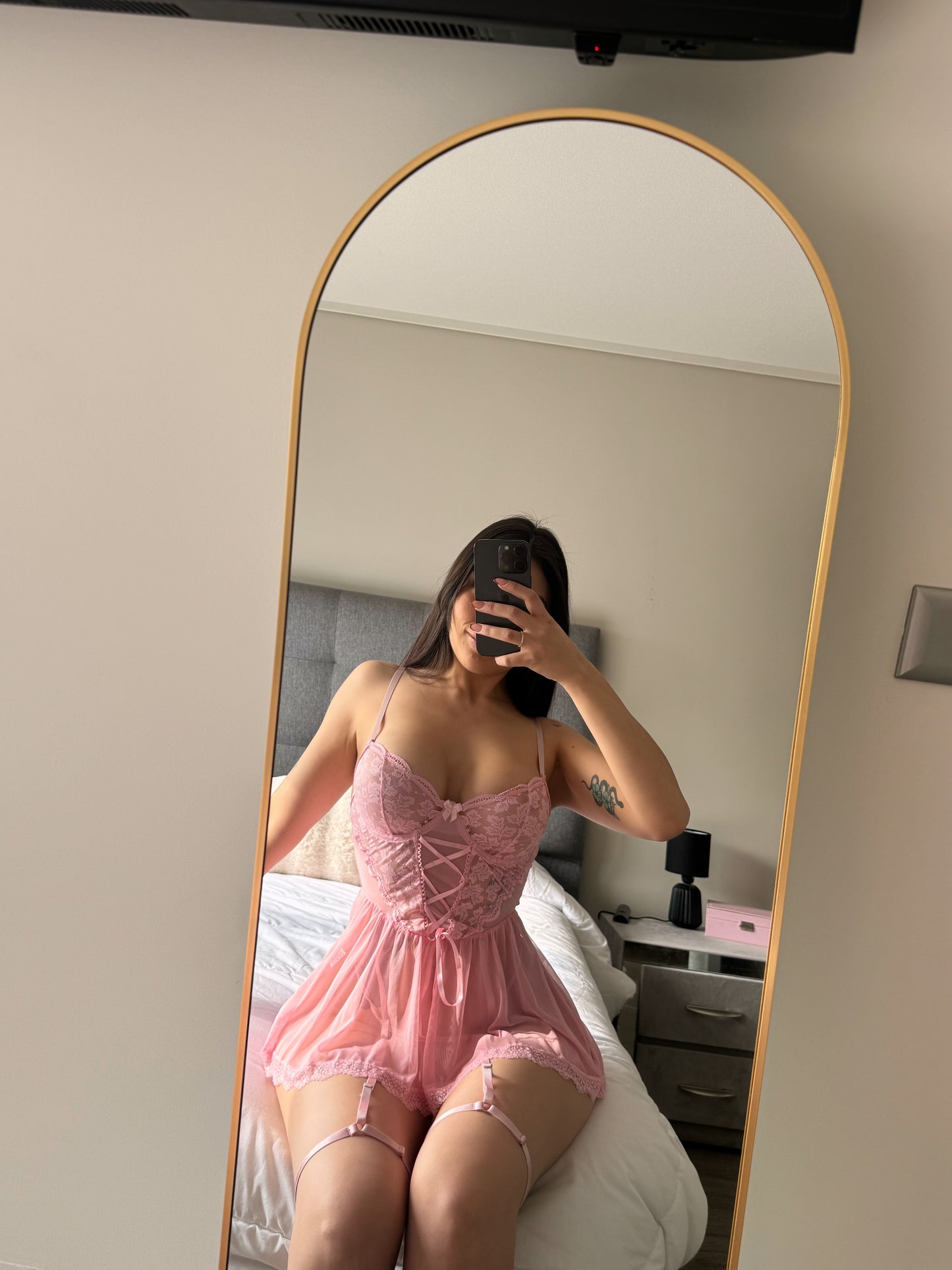 Modelop sentada en una cama celular y espejo usando Babydoll encaje rosado cintas y porta ligas encanto cavrini 