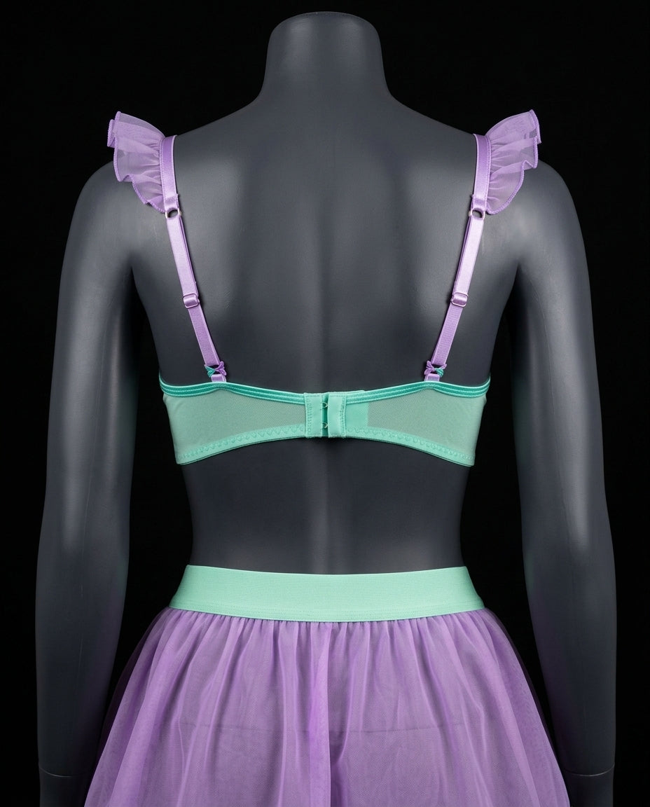 Vista trasera del set de lencería Atlántida en tono verde turquesa y morado sobre maniquí, mostrando la espalda del bralette con tirantes de vuelos y minifalda de tul lila.